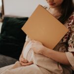Kobieta w ciąży siedzi na sofie i trzyma złoty album na czas ciąży